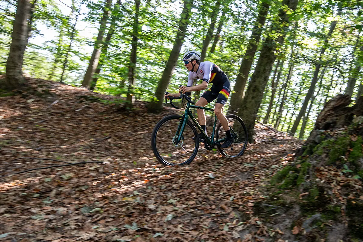 Gravelbike-Fahrer im Deutschlandtrikot auf grünem Gravelbike im dichten Wald.
