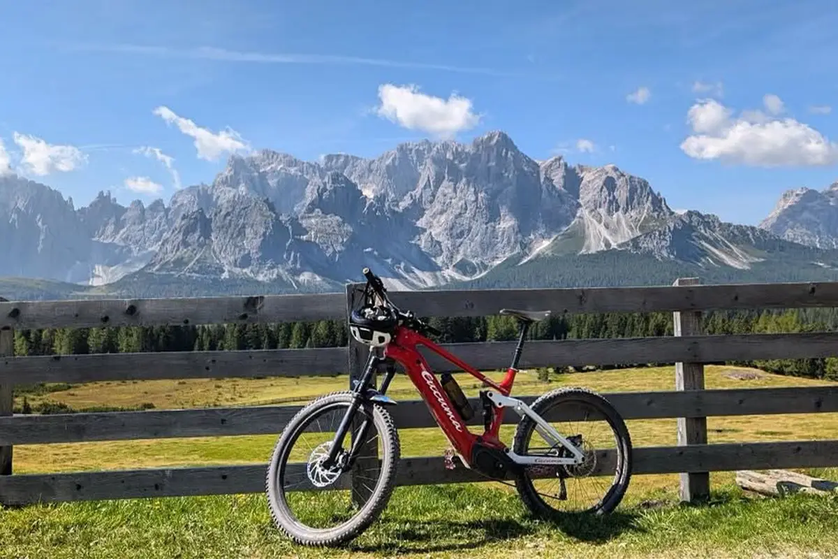 Rotes E-Fully Mountainbike lehnt an einem Holzzaun mit Panoramablick auf felsige