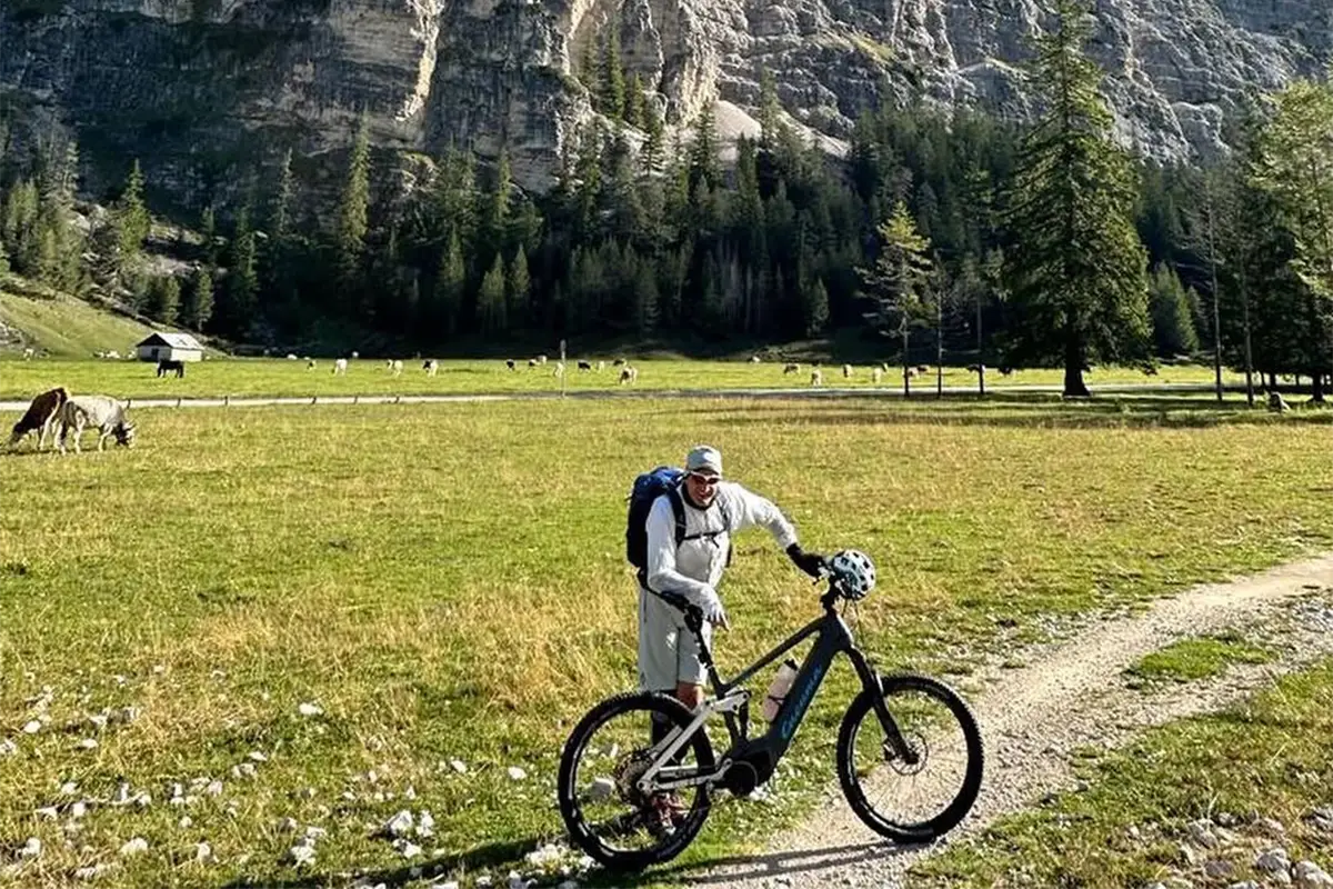 Mann mit grauem E-Fully Mountainbike vor Felswand und Almwiese. Titel: E-Fully in alpiner Landschaft