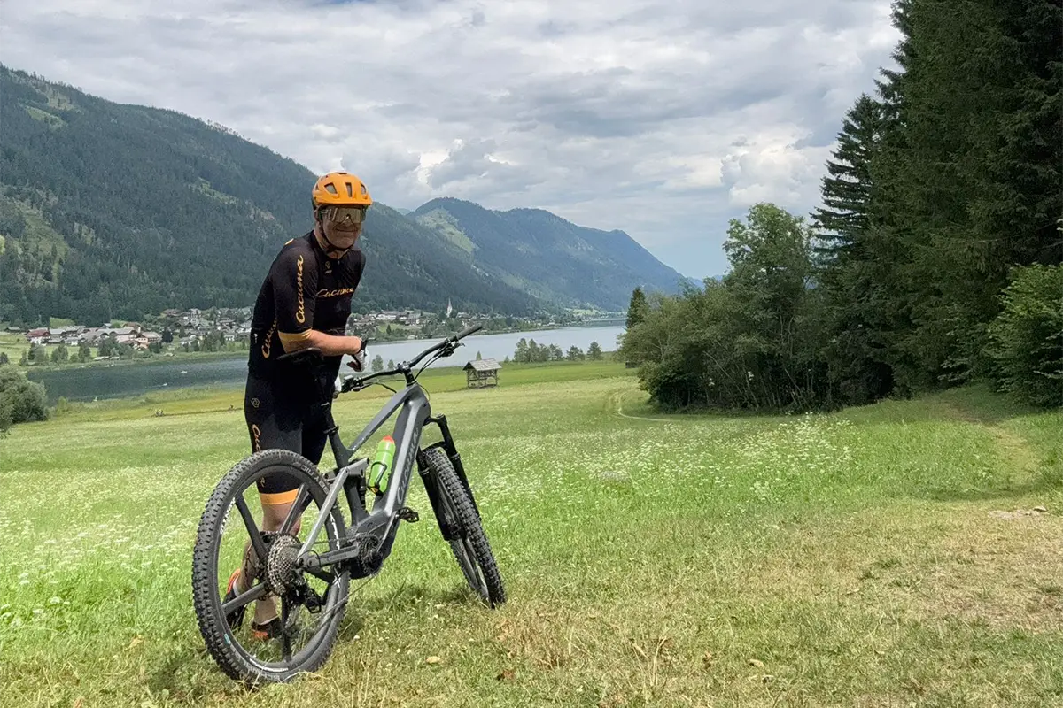 Radfahrer mit grauem E-Fully Mountainbike blickt auf See und Berge.
