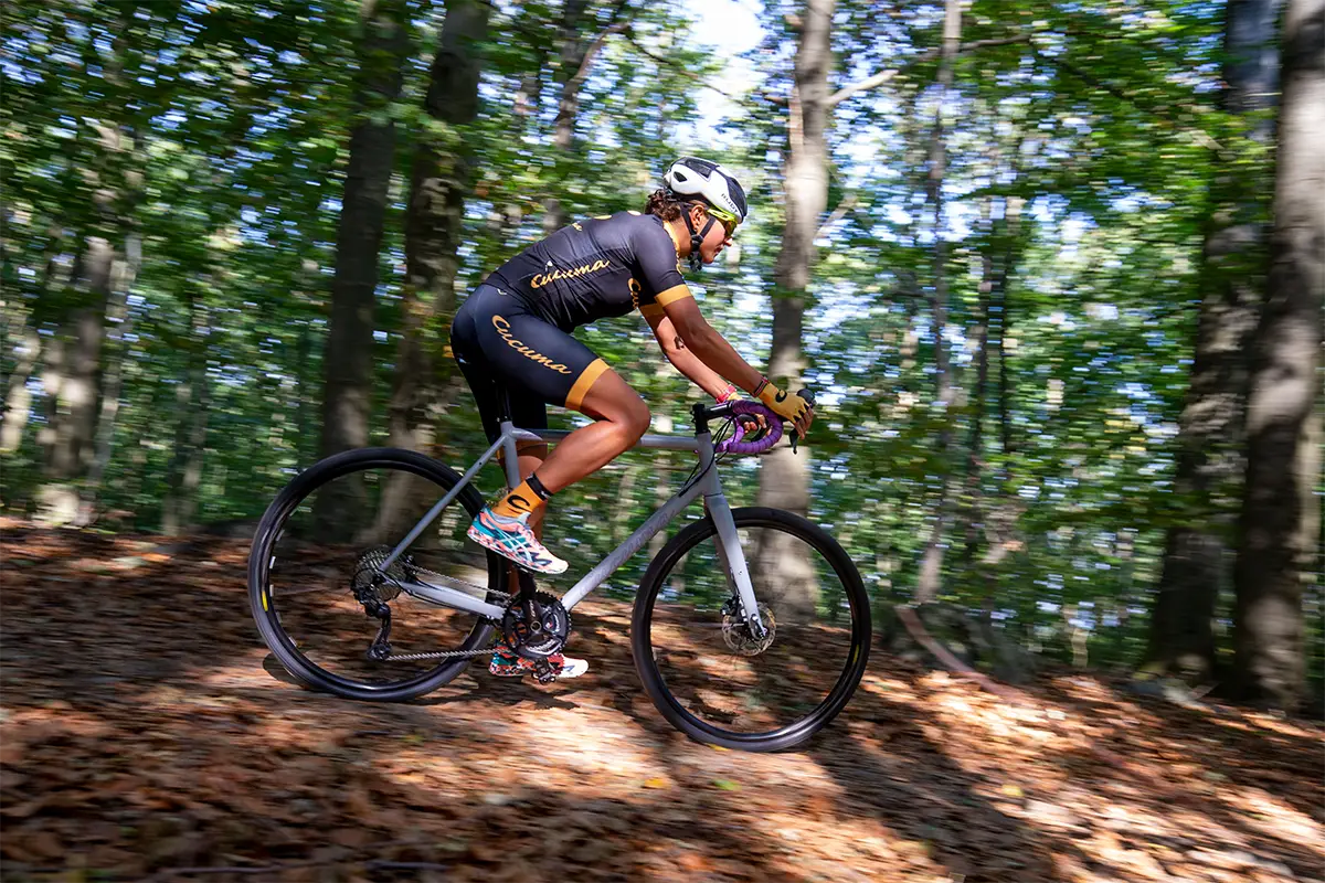 Frau auf einem Gravel Bike fährt durch einen herbstlichen Wald mit Laub am Boden